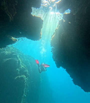 A diver in a deep blue cavern with shafts of light